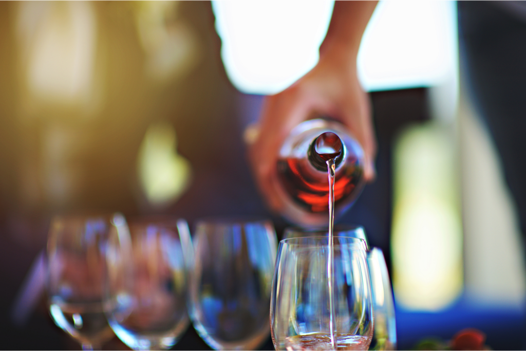 A hand pouring red wine into a glass.