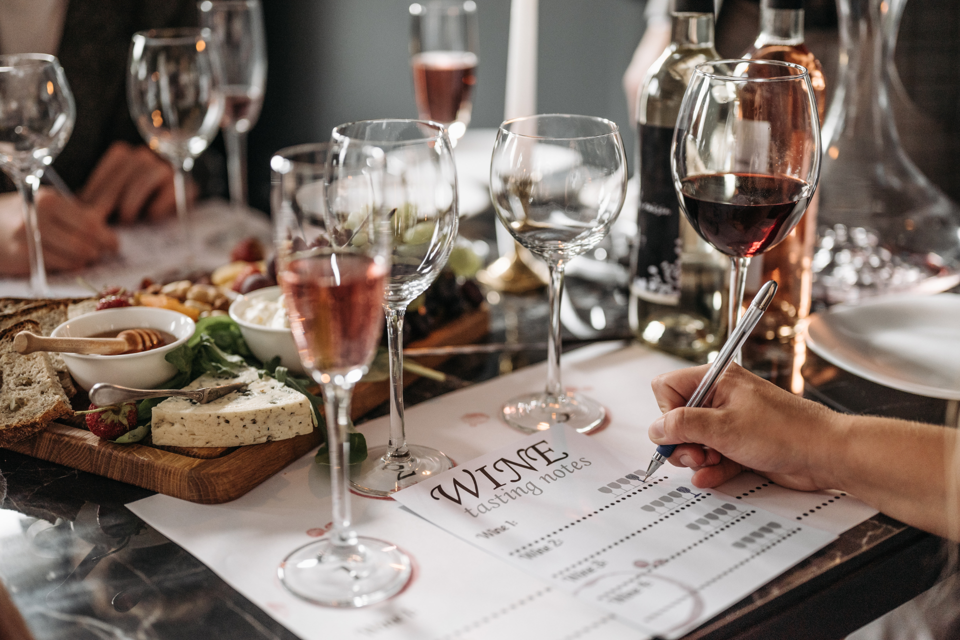 An arranged tasting with wine glasses and labeled cheese pairings on a rustic table in natural light.