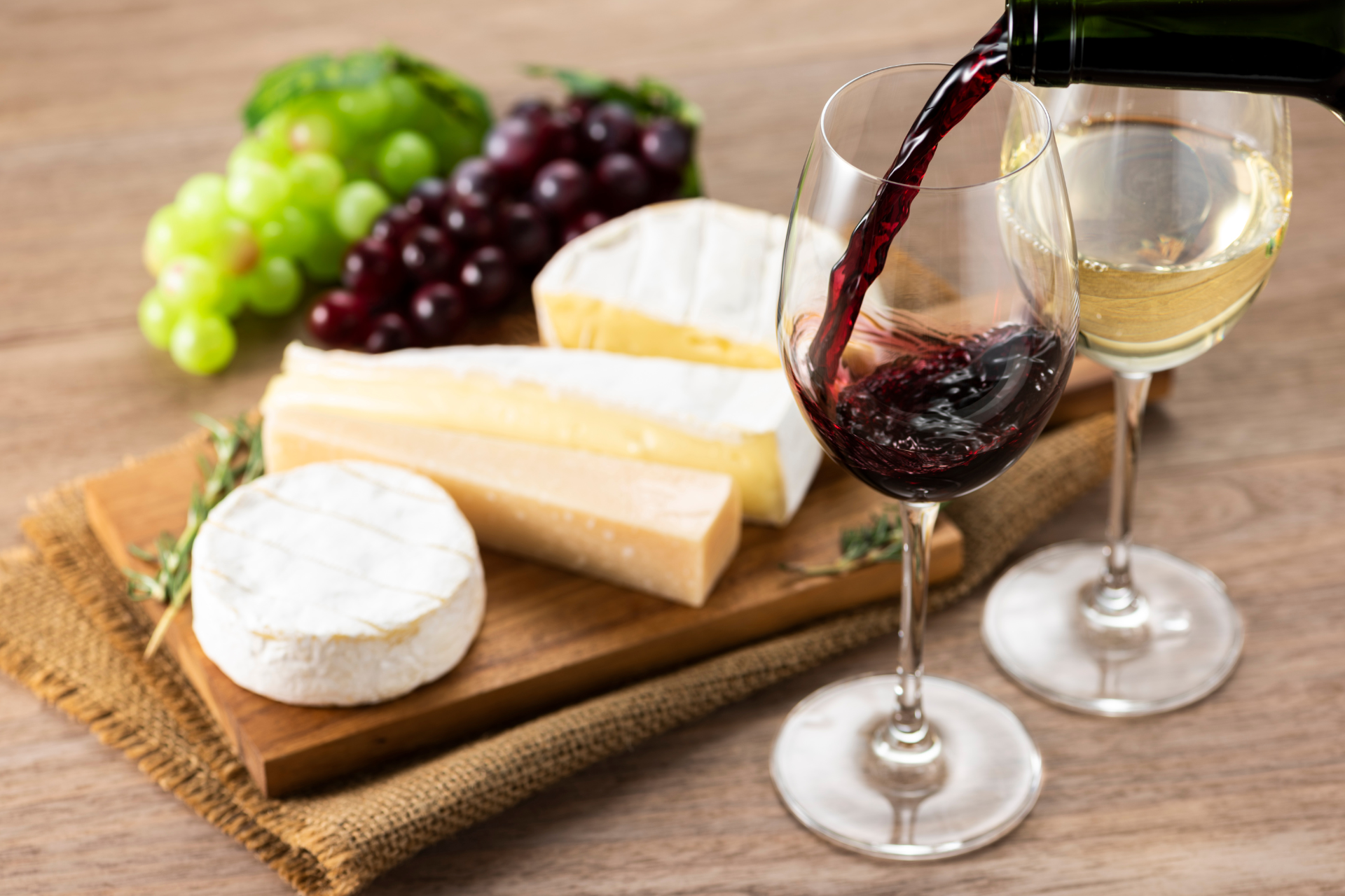 Red wine being poured into a glass next to a board of cheese and grapes
