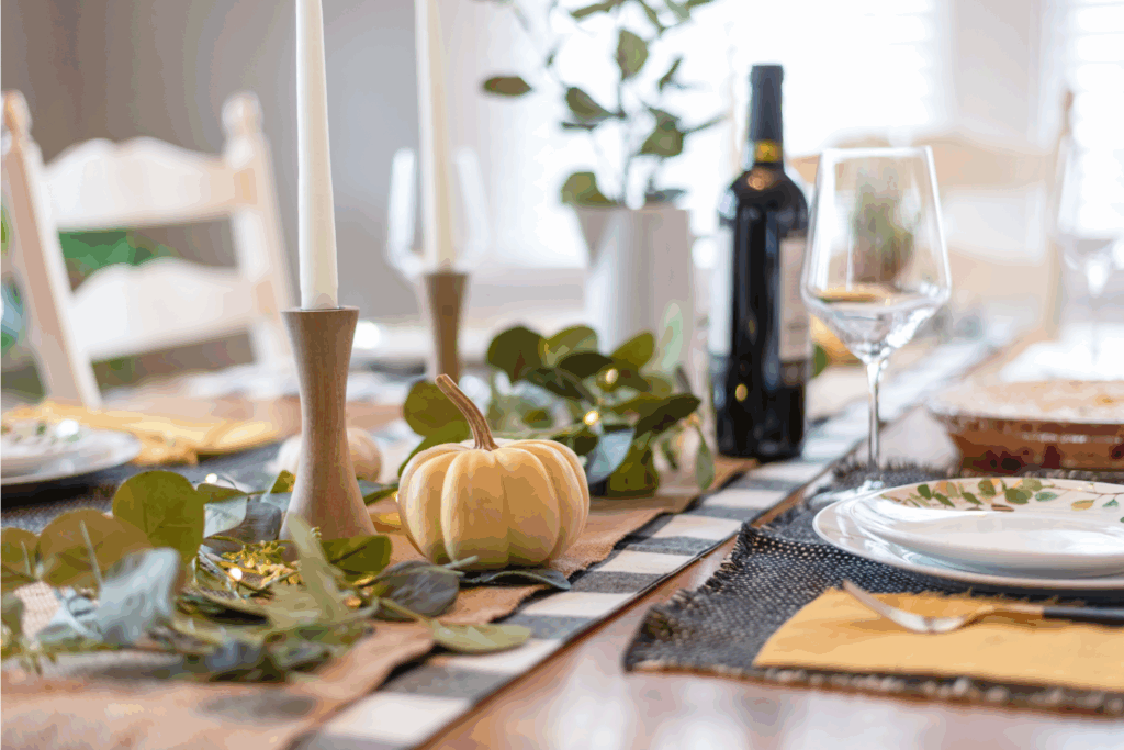 A table decorated in fall decor with pumpkins, eucalyptus, candles and wine