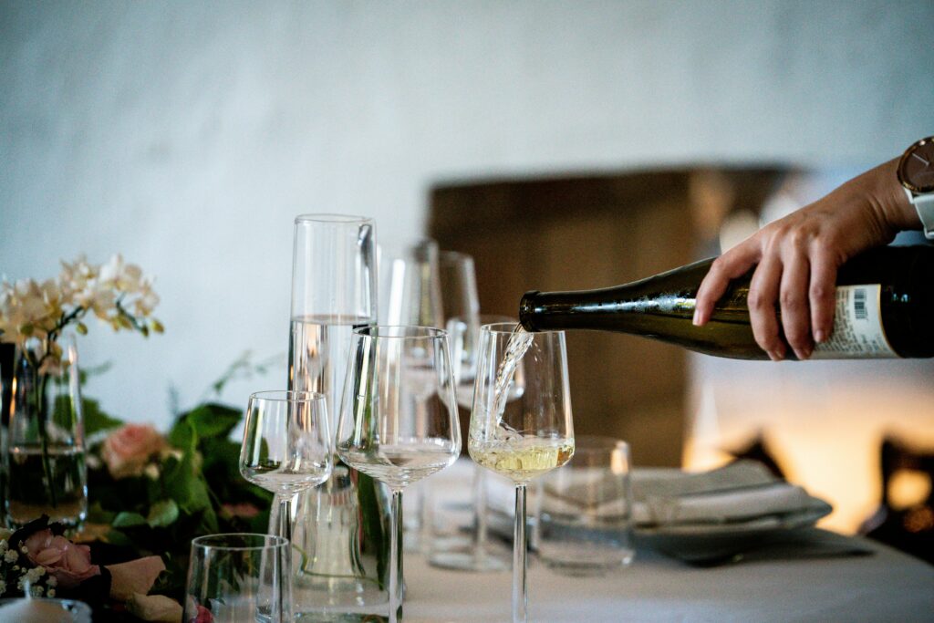 A hand pouring a bottle of white wine into different sized glasses